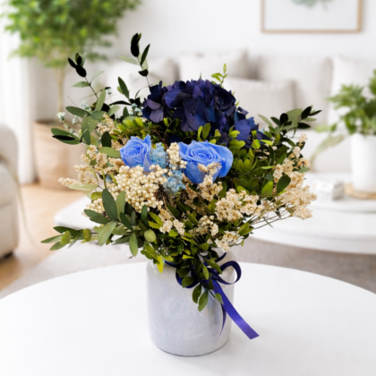 Centro de mesa con rosas azules y hortensia azul oscuro en jarrón azulado.