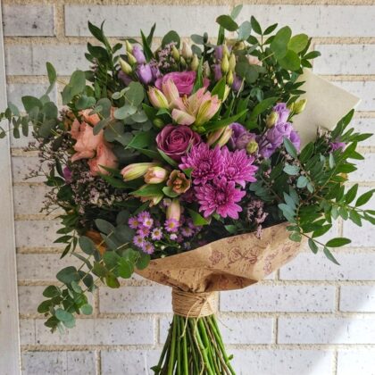 Ramo de flores romántico con rosas malvas, crisantemos púrpura y eucalipto sobre fondo de pared de ladrillo blanco.