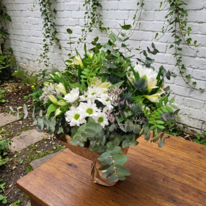 Ramo de flores blancas con margaritas y eucalipto en papel kraft sobre mesa de madera.